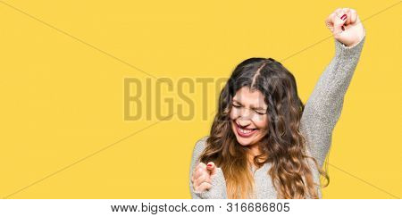 Young beautiful woman wearing winter dress very happy and excited doing winner gesture with arms raised, smiling and screaming for success. Celebration concept.