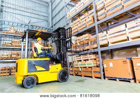 Asian fork lift truck driver lifting pallet in storage warehouse