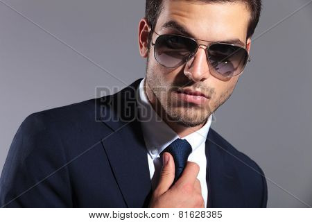 Close up image of a young elegant business man wearing sunglasses, fixing his tie.