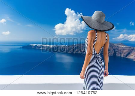 Luxury travel vacation woman looking at view on Santorini famous Europe travel destination. Elegant young lady living fancy jetset lifestyle wearing dress on holidays. Amazing view of sea and Caldera.