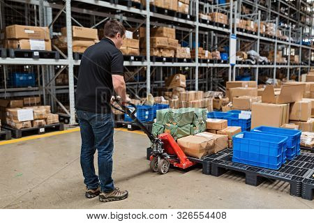 Warehouse Worker Dragging Hand Pallet Truck Or Manual Forklift With The Shipment Pallet Unloading In