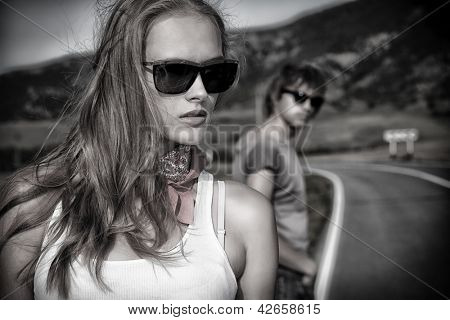 Couple of modern young people posing on a road over picturesque landscape.