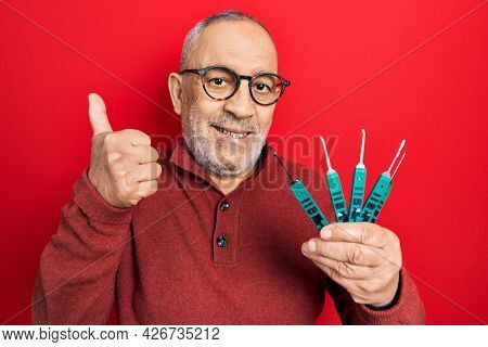 Handsome mature man holding picklock to unlock security door smiling happy and positive, thumb up doing excellent and approval sign 