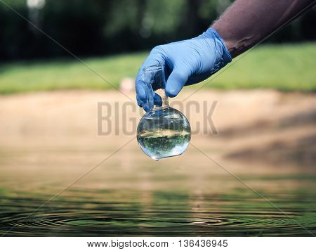 Water sample. Hand in glove holding a retort with clear water. Concept - water purity analysis environment ecology. Water testing for infections permission to swim