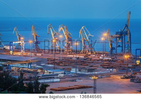 Sea commercial port at night in Mariupol Ukraine. Industrial view. Cargo freight ship with working cranes bridge in sea port at twilight. Cargo port logistic