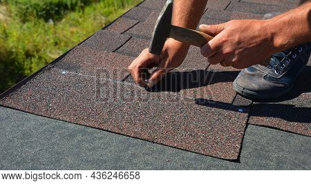 A Close-up Of Asphalt Shingles Installation On The Roof Edge. A Roofer Is Nailing Asphalt Shingles T