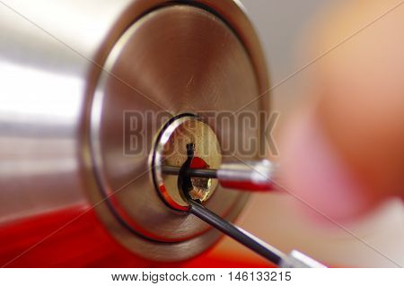 Closeup hands of locksmith using metal pick tools to open locked door.