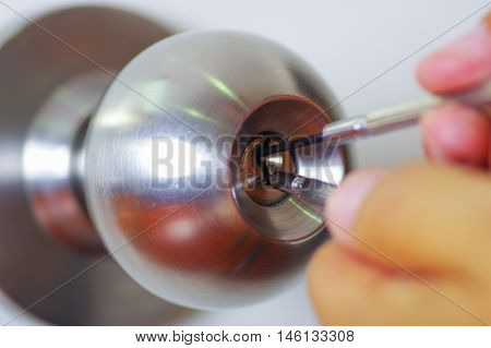 Closeup hands of locksmith using metal pick tools to open locked door.