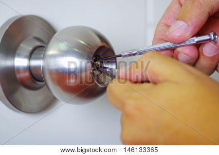 Closeup hands of locksmith using metal pick tools to open locked door.