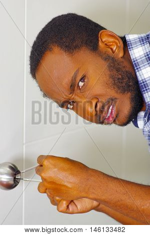 Closeup head and hands of locksmith using pick tools to open locked door, looking at camera with frustrated facial expression.