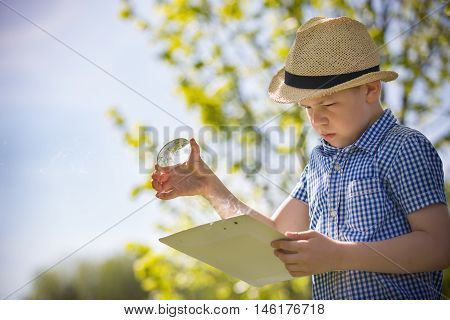 Adorable kid boy making fire on paper with a magnifying glass outdoors on sunny day. Child exploring fire nature in the garden. Young explorer with magnifier. Education and discovery concept