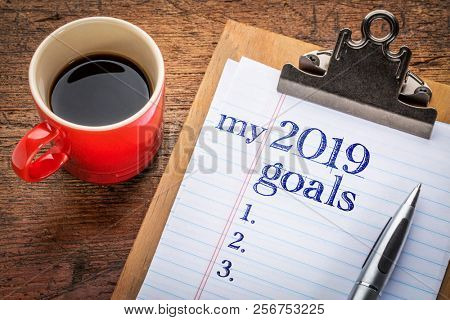 my 2019 goals list on clipboard and coffee against grunge wood desk