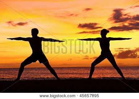 Pessoas de ioga treinando e meditando em pose de guerreiro fora pela praia ao nascer ou o pôr do sol. Mulher e