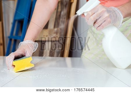 Person doing fine cleaning of white table with liquid spray and yellow wisp