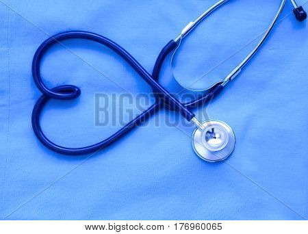 Medical stethoscope twisted in heart shape lying on patient medical history list and blue doctor uniform closeup. Medical help or insurance concept. Cardiology care, health, protection and prevention.