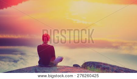 Young Woman Sitting Enjoying Peaceful Moment Of Beautiful Colorful Sunset. In The Reflection Of The