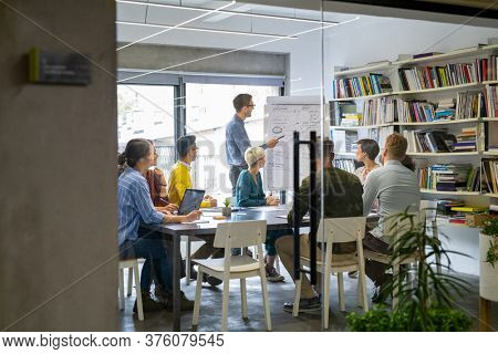 Businessman giving a presentation to multiethnic creative team at office. Business brief with annual goals with employees. Leadership man training businessmen and businesswomen in conference room.