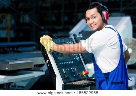 Worker entering data in CNC machine at factory floor to get the production going