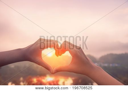 Female hands in the form of heart against sunlight with mist in blue sky Hands in shape of love heart - Love concept.