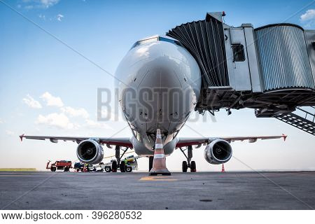 A White Passenger Aircraft At The Jet Bridge And Is Loaded With Baggage