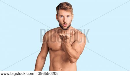 Young caucasian man standing shirtless looking at the camera blowing a kiss with hand on air being lovely and sexy. love expression. 