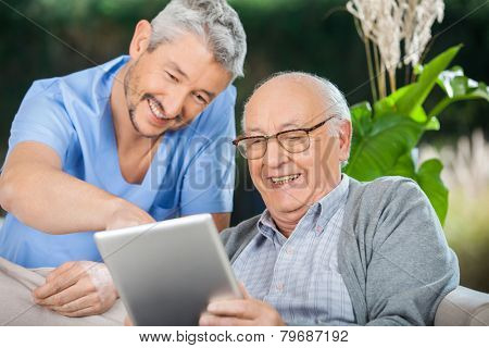 Happy male nurse and senior man enjoying while using tablet computer in nursing home porch