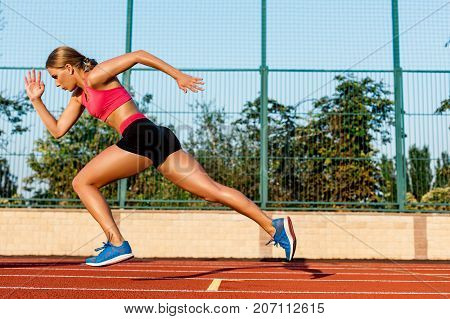 Runner sprinting towards success on run path running athletic track. Goal achievement concept. Female athlete sprinter doing a fast sprint for competition on red lane at an outdoor field stadium.