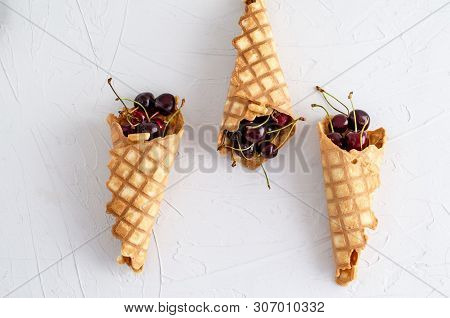 Ice Cream Cone Filled With Cherries On A Light White Concrete Background.