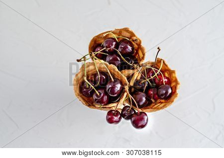 Three Ice Cream Cones Filled With Cherries In A Glass Beaker On A Light White Concrete Background.