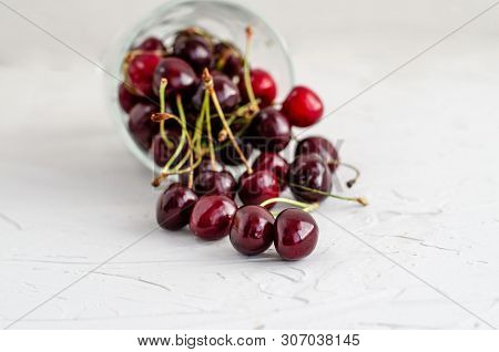 Ripe Fresh Red Sweet Cherry Poured From An Inverted Glass Cup On A White Concrete Background