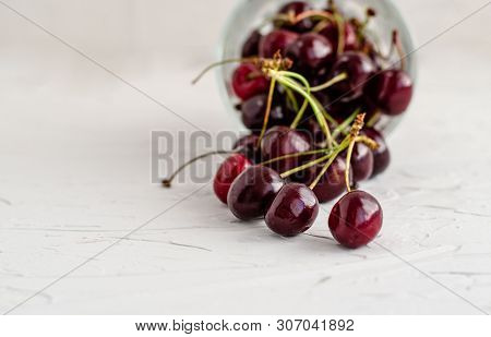 Ripe Fresh Red Sweet Cherry Poured From An Inverted Glass Cup On A White Concrete Background