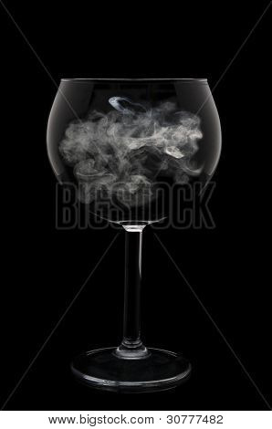 A Wine Glass with a wisp of smoke in the bowl over a black background.