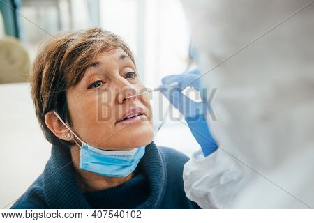 Close Up Of The Face Of Senior Female Patient Being Tested For Covid-19 With A Nasal Swab, By A Heal