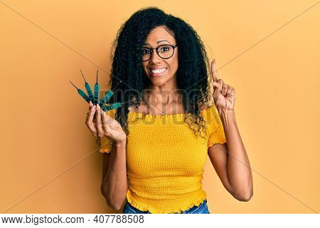 Middle age african american woman holding picklock to unlock security door smiling with an idea or question pointing finger with happy face, number one 