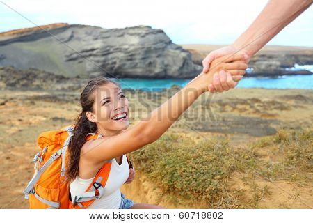 Helping hand - hiker woman getting help on hike smiling happy overcoming obstacle. Tourist backpackers walking on Green Sand Beach, Papakolea on Big Island, Hawaii, USA. Young couple traveling.