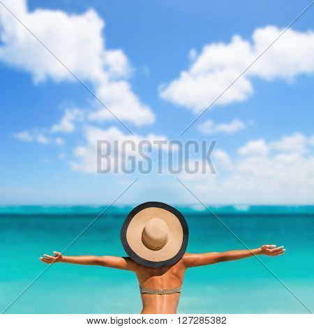 Summer vacation happiness carefree joyful sun hat woman with open arms in success enjoying tropical beach destination. Holiday bikini girl relaxing from behind on Caribbean vacation. Sky copyspace.