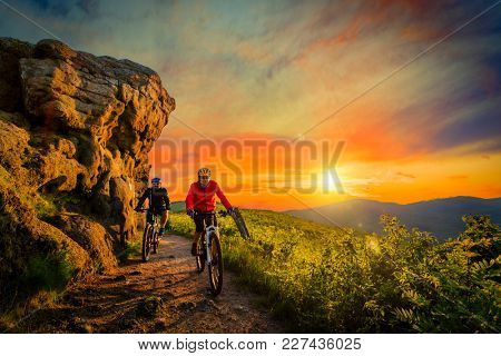 Mountain biking women and man riding on bikes at sunset mountains forest landscape. Couple cycling MTB enduro flow trail track. Outdoor sport activity.