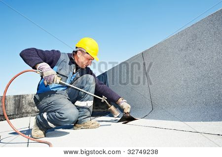 Roofer installing Roofing felt with heating and melting roll of bitumen roll by torch on flame