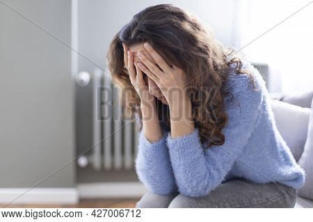 Young Depressed Woman Sitting On Sofa In Living Room. She Feeling Sad And Worried Suffering Depressi