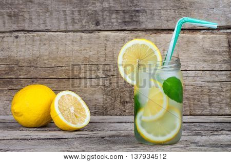 Summer fruit drink on wooden background. Cold lemonade with ice. Detox citrus infused flavored water. Refreshing summer homemade cocktail with lemon. Fresh lemon and lemonade on wooden background