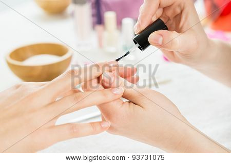 Closeup shot of a beautician applying nail polish to female nails. Woman getting nail manicure. Shallow depth of field with focus on nail polish.
