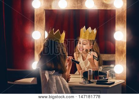 Cute little actress. Child girl in Princess costume on the background of theatrical scenes and mirrors.