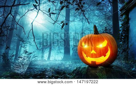 Glowing Jack o lantern in a creepy old overgrown cemetery with cool blue moonlight