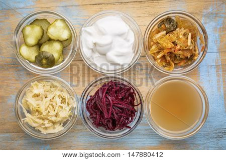 a set of fermented food great for gut health - top view of glass bowls against grunge wood:  cucumber pickles,  coconut milk yogurt, kimchi, sauerkraut, red beets, apple cider vinegar