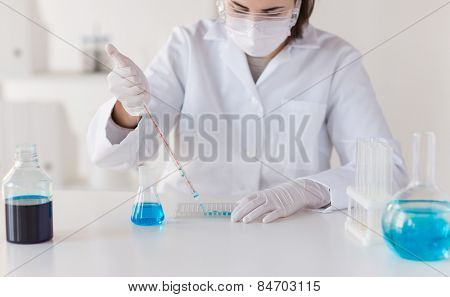 science, chemistry, biology, medicine and people concept - close up of young female scientist with pipette and flask making test or research in clinical laboratory