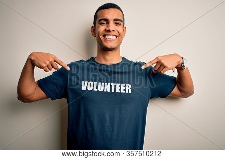 Young handsome african american man volunteering wearing t-shirt with volunteer message looking confident with smile on face, pointing oneself with fingers proud and happy.