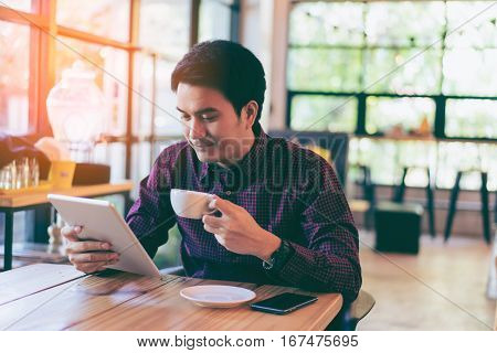 Young Asian Handsome Businessman Smiling While Reading His Tablet