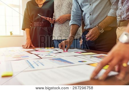 Businessmen and businesswomen discussing graphs showing results of successful teamwork. Group of business people having meeting together. Closeup of multiethnic business hands analyzing charts.