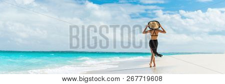 Luxury travel summer beach vacation woman walking in black beachwear skirt and hat on paradise white sand Caribbean beach. Lady tourist on Caribbean holiday vacation resort. Banner panorama landscape.