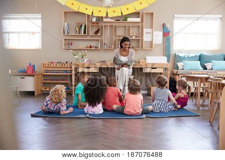 Teacher At Montessori School Reading To Children At Story Time